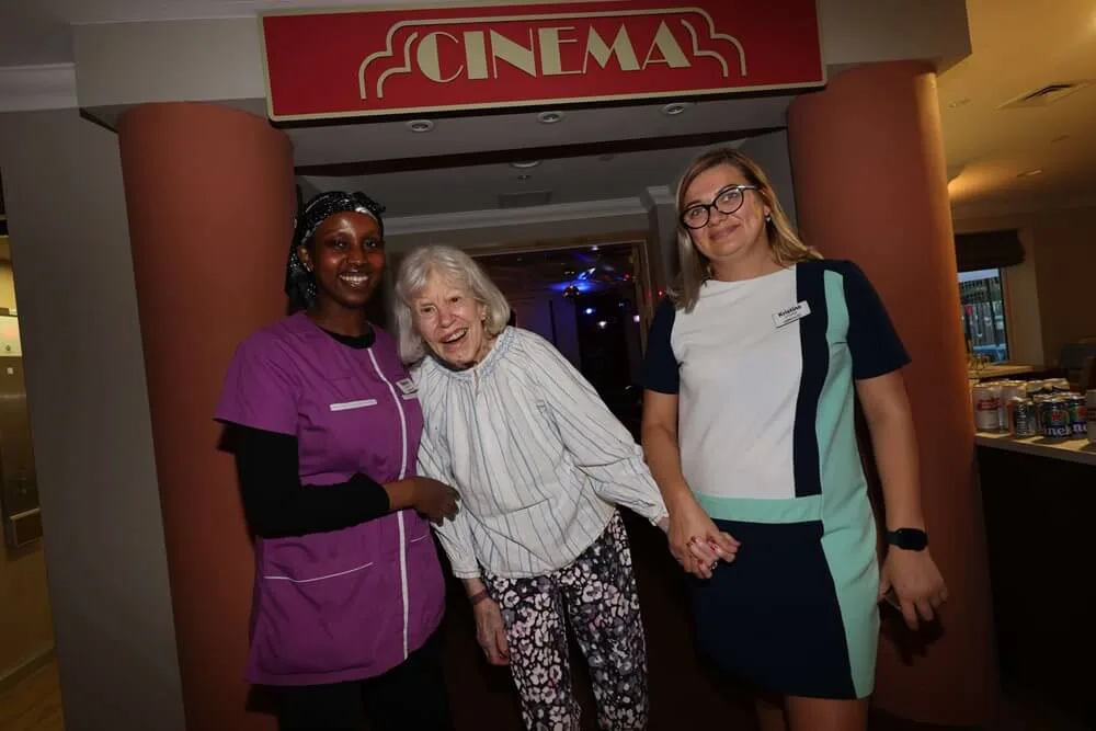 Two members of staff and a smiling resident under a red Cinema sign at Sherwood Grange